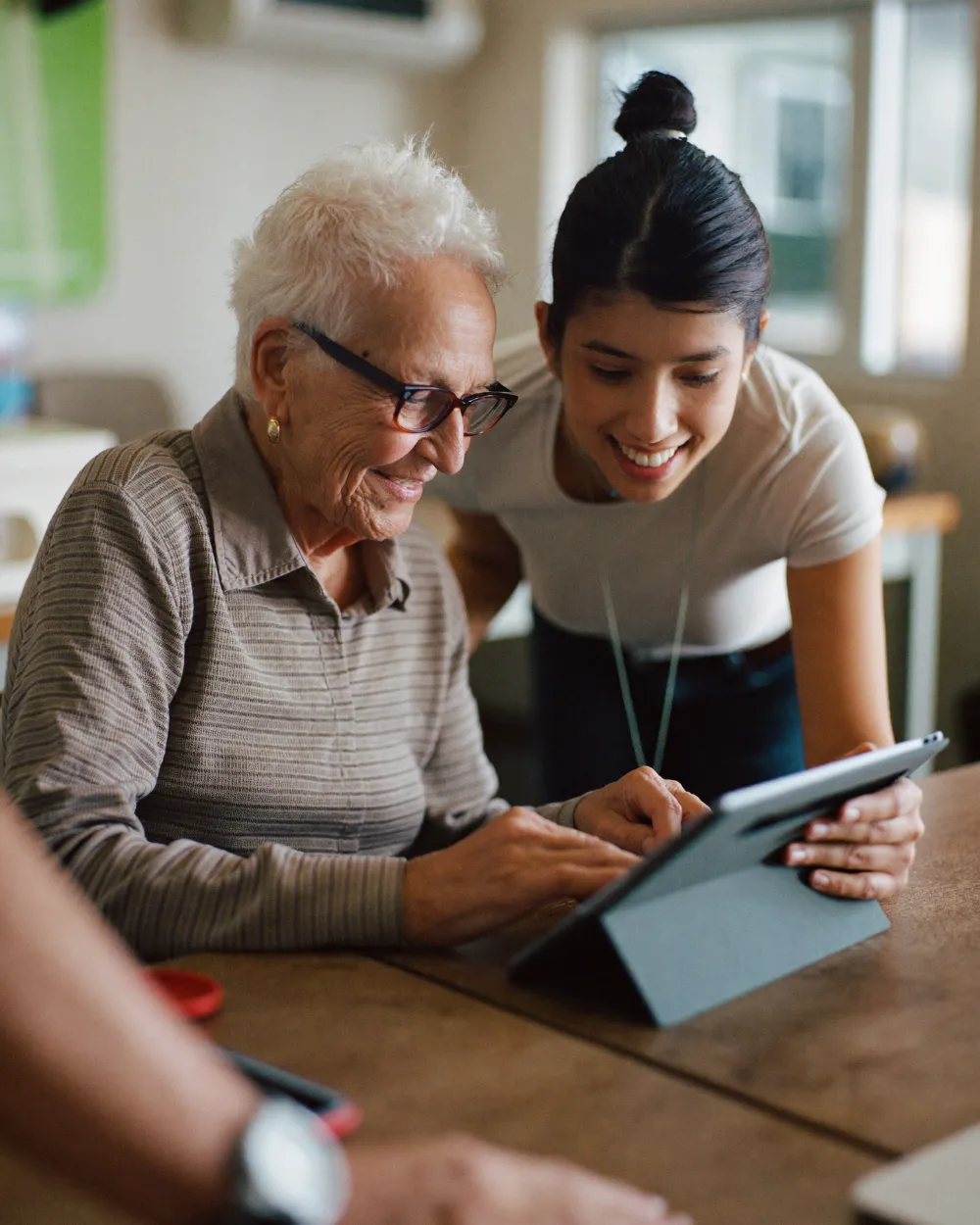 An older woman learning to use a tablet with a smiling staff member